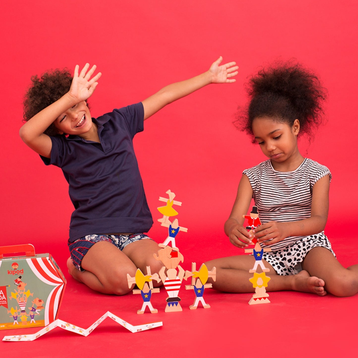 Kipod Toys ‘Ta-Da’ Balancing Circus | Hand-Crafted Wooden Toy | Wooden Stacking and Balancing Game | Lifestyle – Boy and Girl Playing, Red Background | BeoVERDE.ie