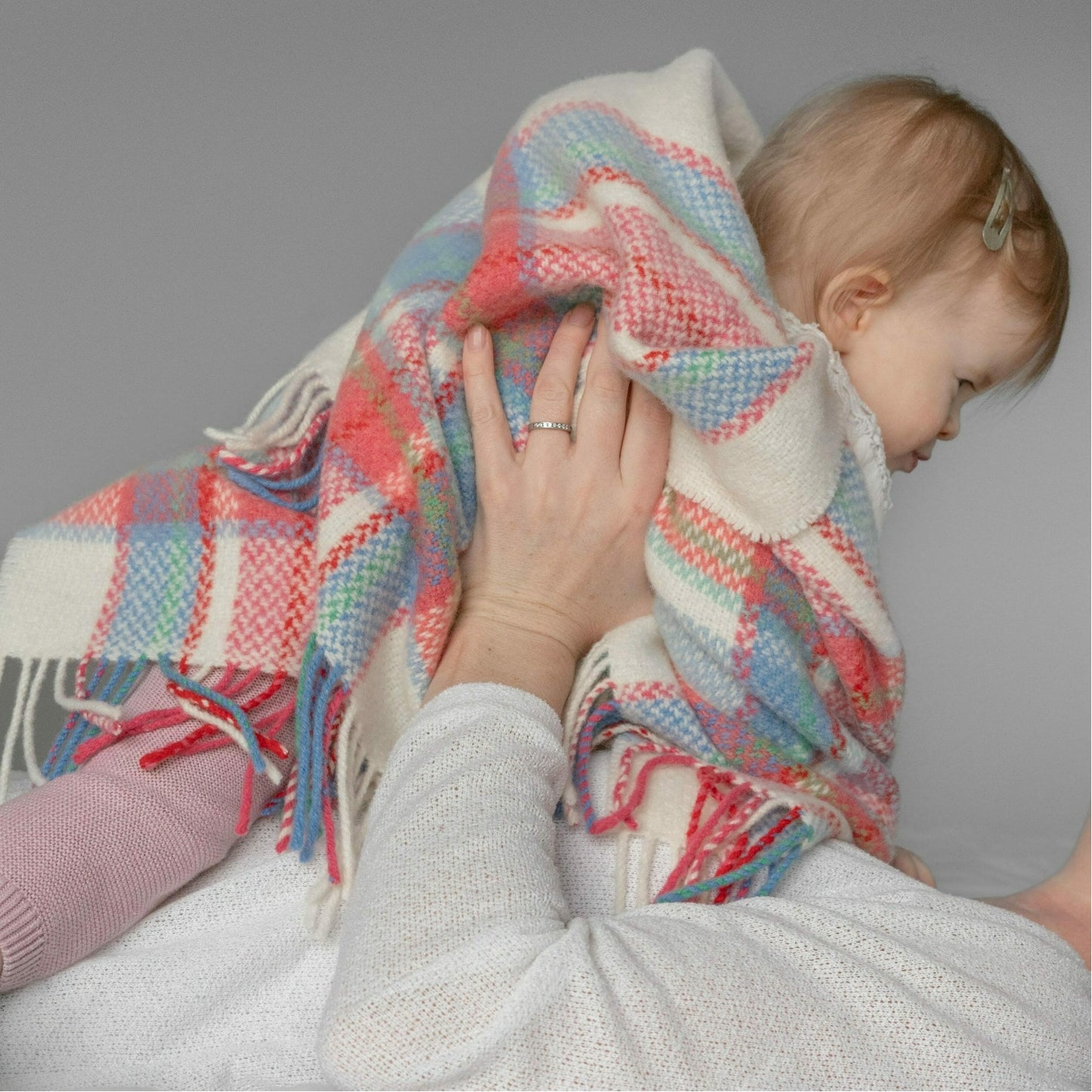 John Hanly Irish Cashmere Baby Blanket | White, Pink & Blue Border Check Pattern | Cashmere Blanket | Lifestyle: Mother Holding Baby | BeoVERDE Ireland