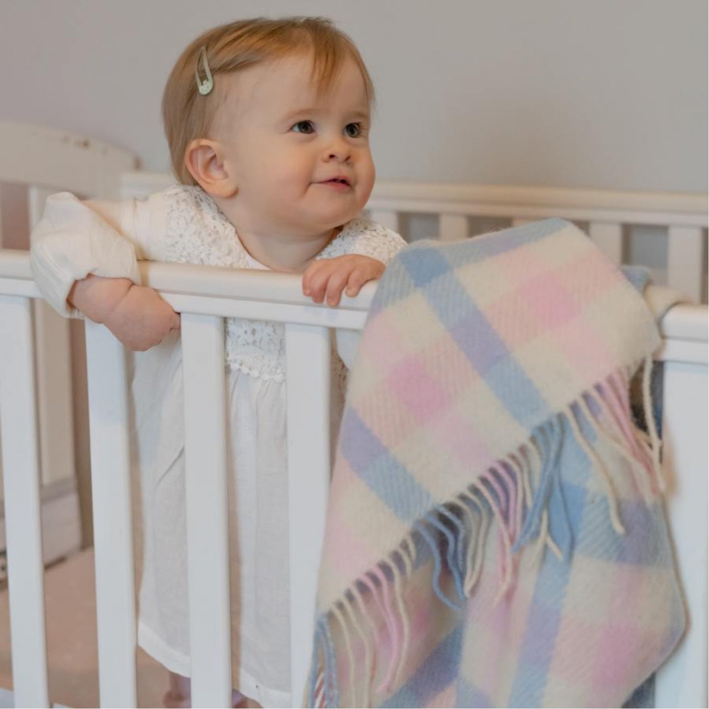 John Hanly Irish Wool Baby Blanket | White, Pink & Blue Border Block Check | 100% Pure Irish Wool Blanket | Lifestyle: Smiling Baby in Bed with Blanket | BeoVERDE Ireland