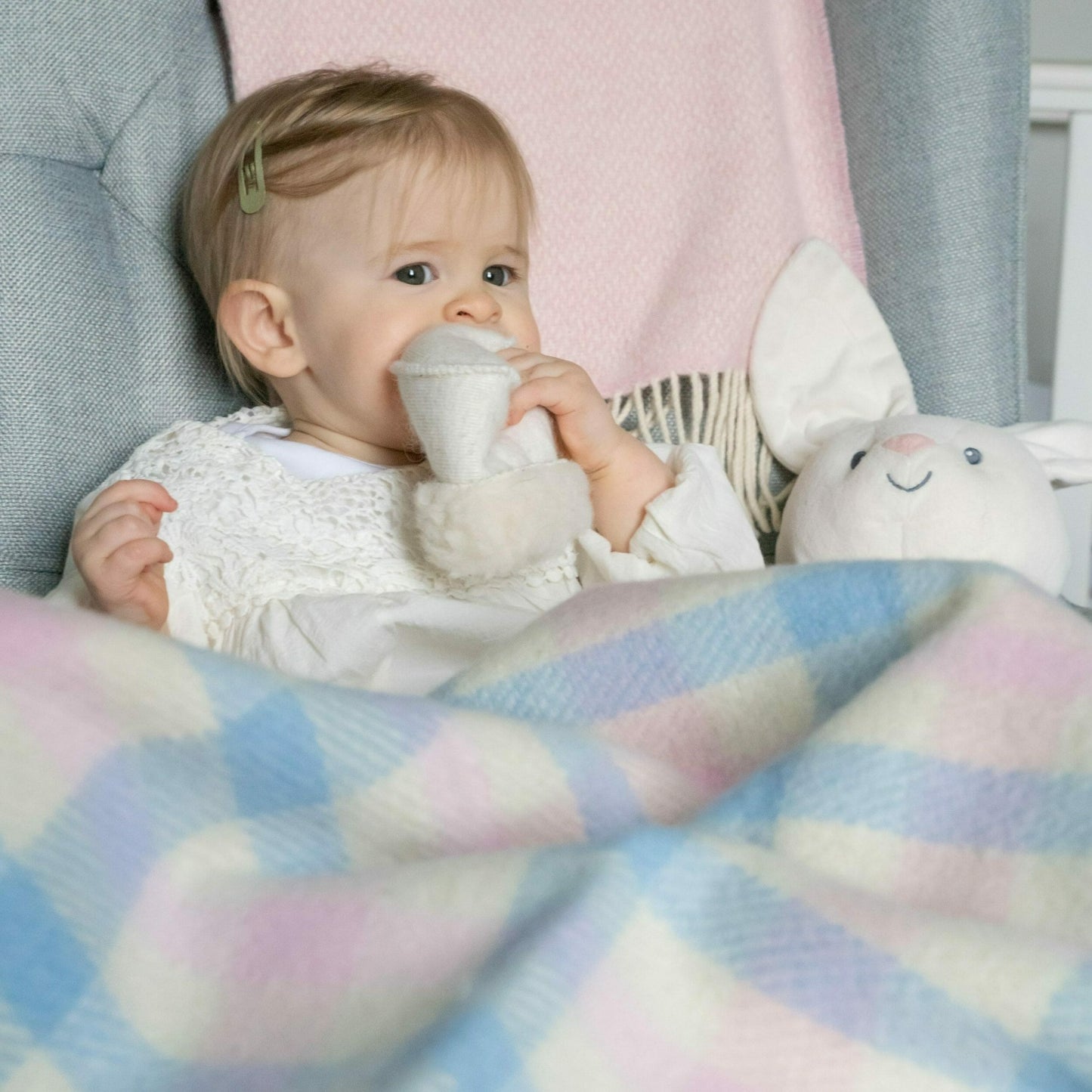 John Hanly Irish Wool Baby Blanket | White, Pink & Blue Border Block Check | 100% Pure Irish Wool Blanket | Lifestyle: Baby on Sofa with Blanket | BeoVERDE Ireland