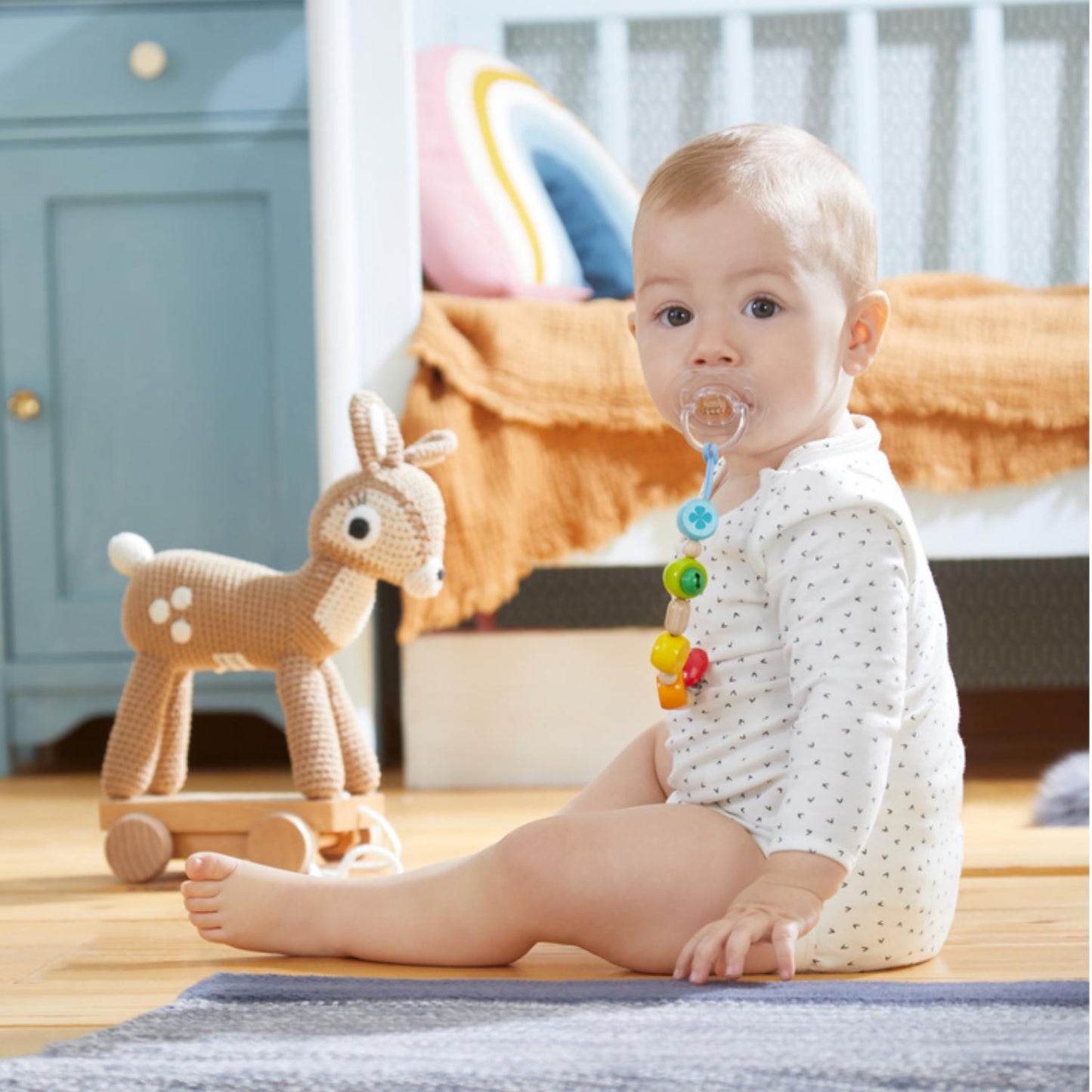 HABA Jingling Bell Wooden Dummy Clip | Lifestyle – Baby with Dummy Clip on Floor with Toy Deer | BeoVERDE.ie